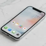 iPhone SE 2026 posé sur une surface en marbre blanc, vue en plongée légère mettant en valeur son design compact et son écran d'accueil